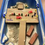 The sand tray with a set up including a cardboard road and wooden toys
