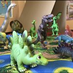 A table covered in an earthy back-drop with various types of dinosaur toys