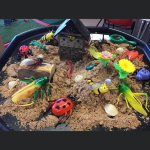 A sand pit filled with various types of large bug toys