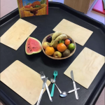 A table set with place mats and cutlery and a bowl of fresh fruit