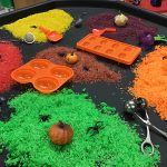 Halloween scene with a tuff tray filled with toy spiders, pumpkins and piles of different colours of rice