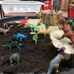 A tuff tray covered in soil and dinosaurs