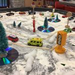 A tuff try covered in fake snow, Christmas trees and cars stuck in the snow